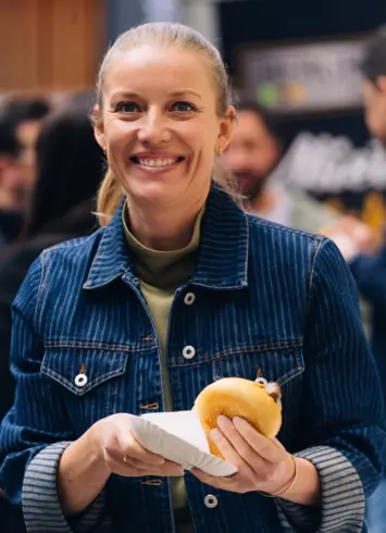 Eine Frau, die ein Bratwurstbrötchen in der Hand hält und lächelt