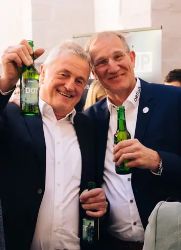Zwei lächelnde Männer, die mit Bierflaschen in die Kamera prosten